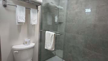 A modern bathroom with a glass-enclosed shower, a toilet, and a towel rack with multiple towels.