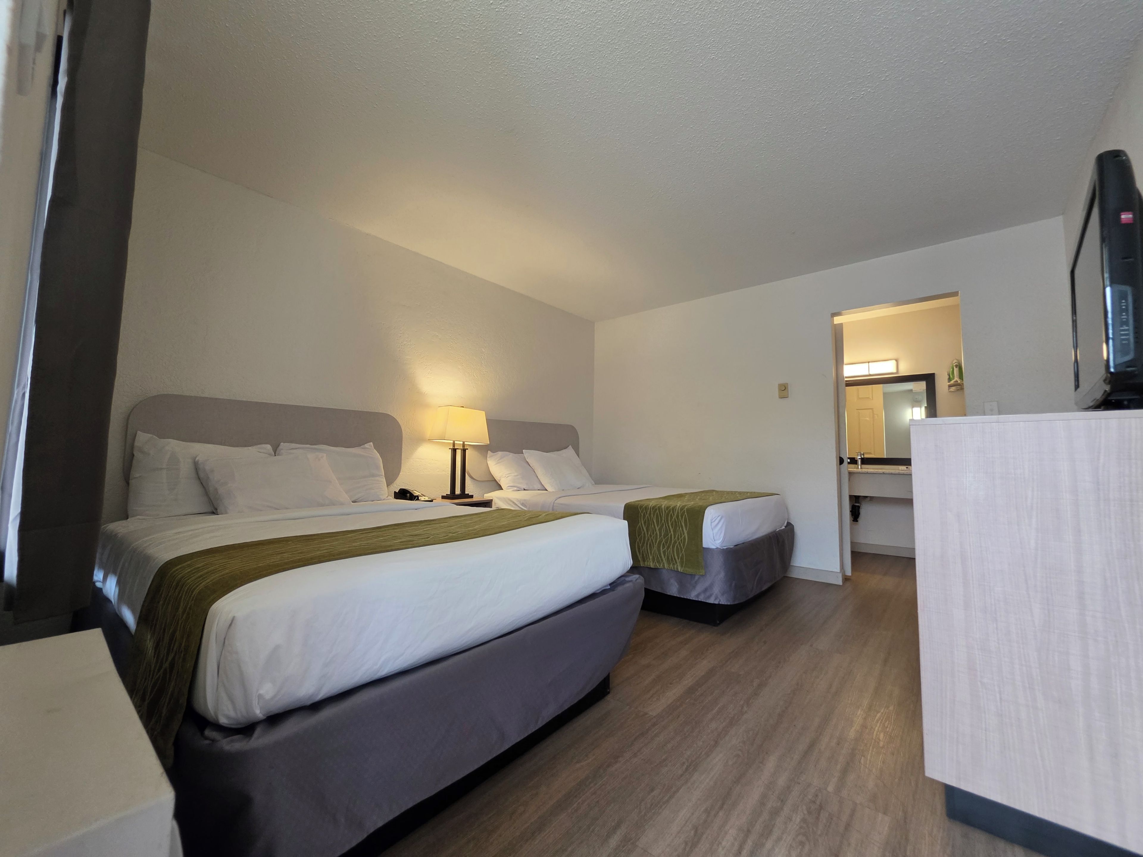 A hotel room with two beds, a bedside table with a lamp, a mirror, and a television.