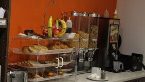 Una estación de desayuno con una tostadora, una cesta de frutas y diversas bollerías.