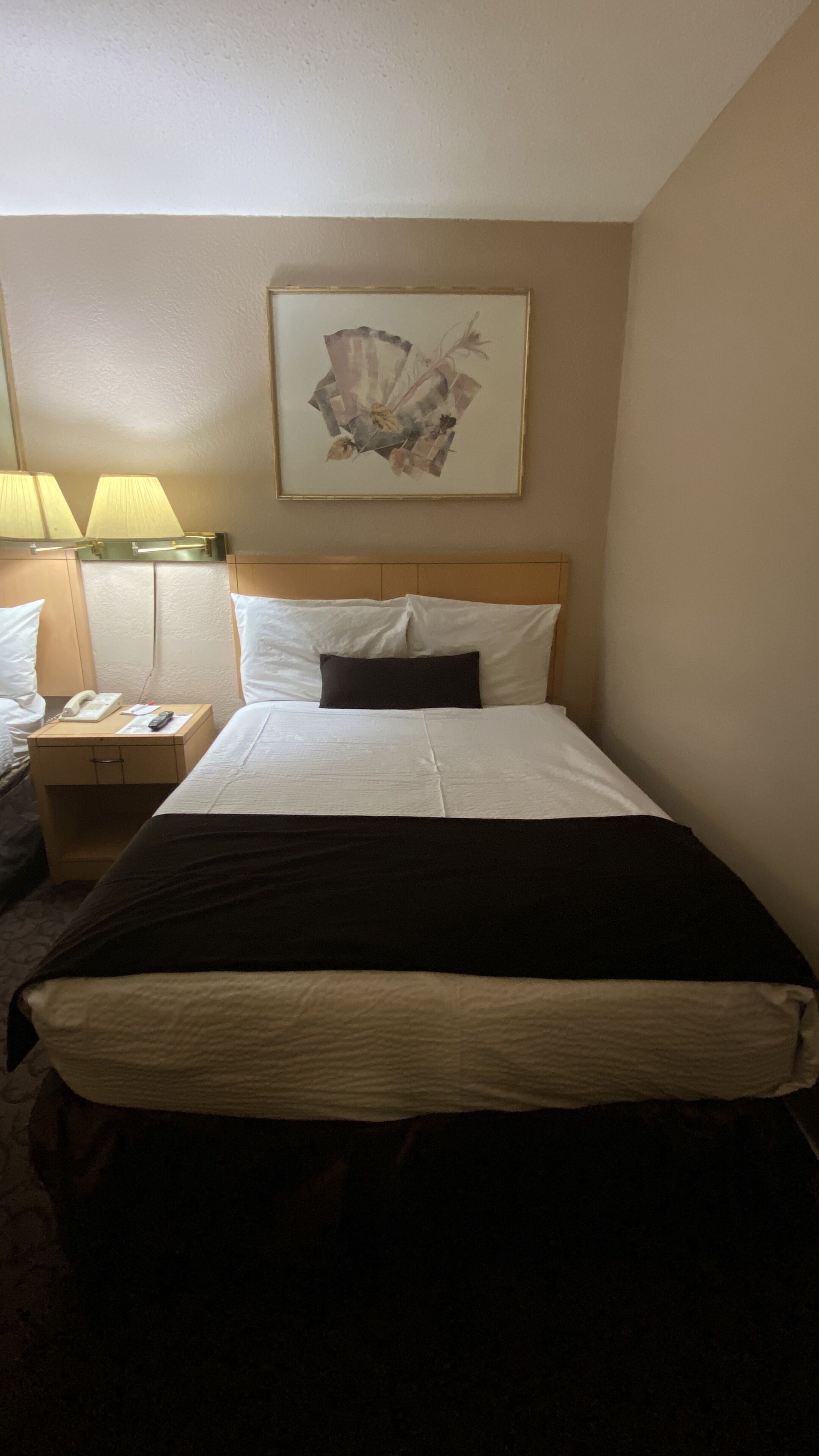 Een hotelkamer met een bed, nachtkastje, lamp en een schilderij aan de muur.