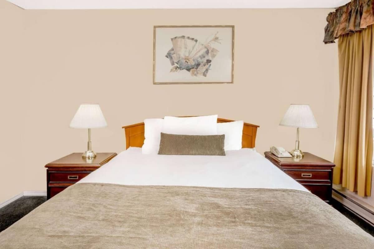 Een hotelkamer met een bed, twee nachtkastjes met lampen, een telefoon en een lijst met kunst aan de muur.
