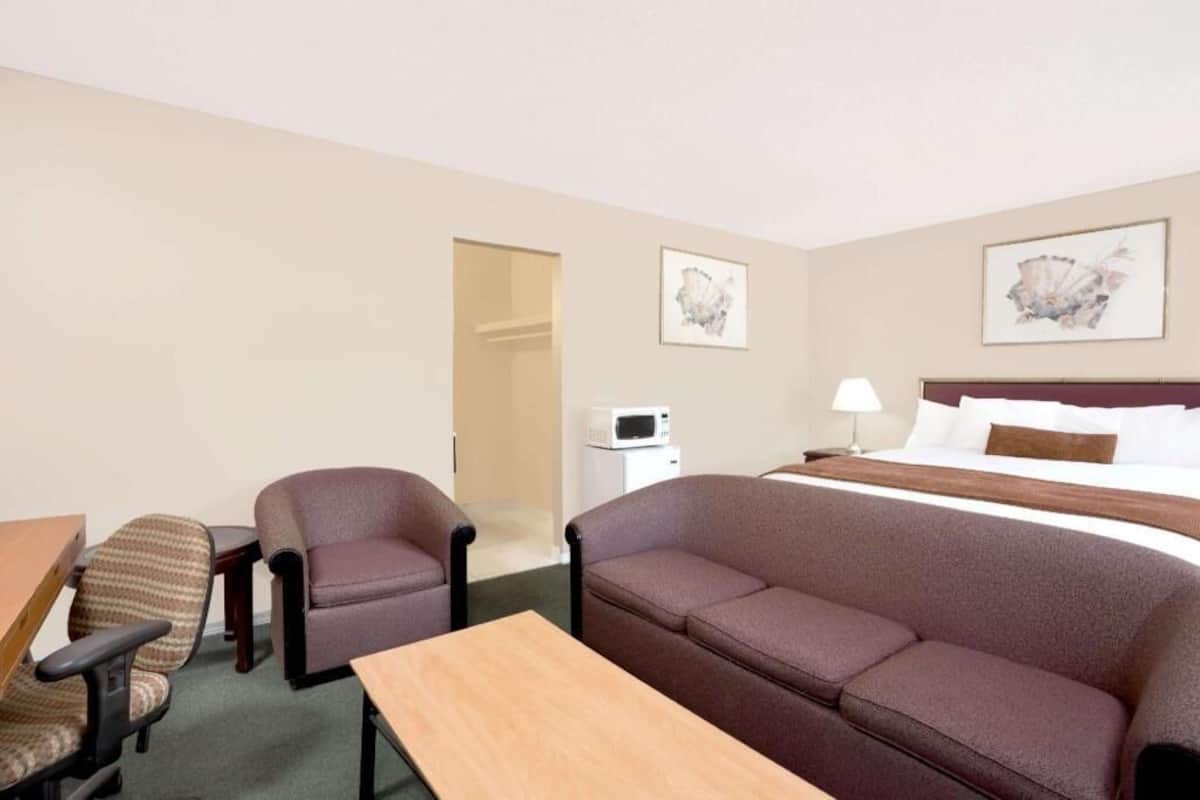 Een hotelkamer met een bed, een bank, een bureau, een stoel, een magnetron en twee ingelijste foto's aan de muur.