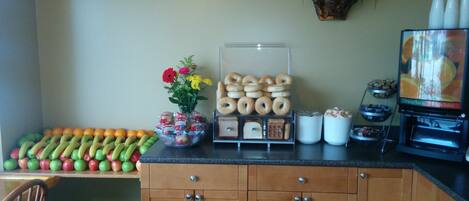 A kitchen counter with a fruit bowl, a vase with flowers, a display of bagels, and a coffee machine.