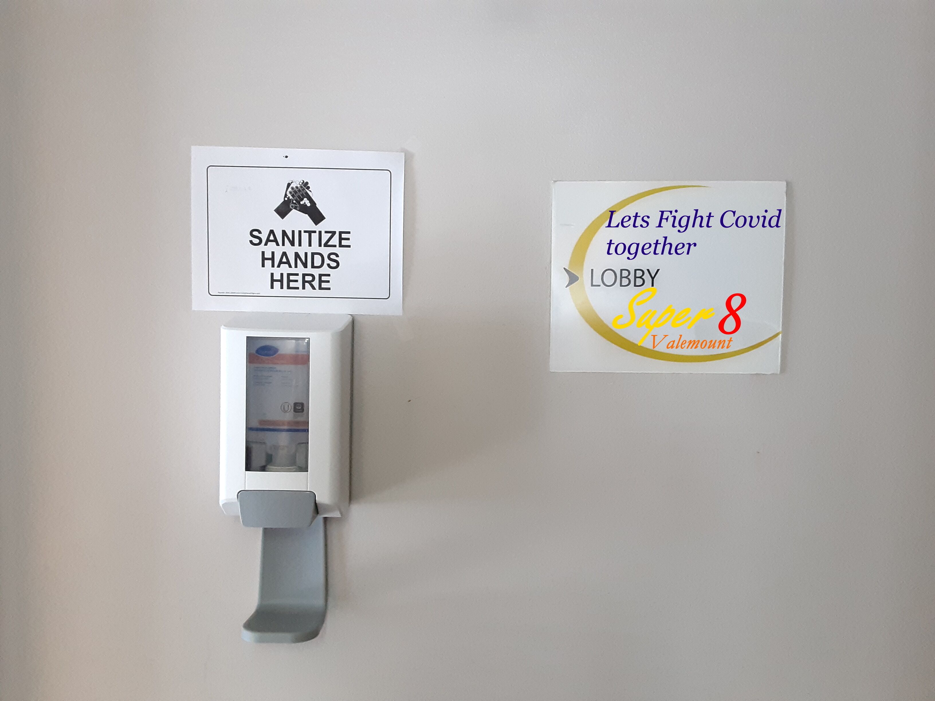 A hand sanitizer dispenser and two signs: one instructing to sanitize hands and another promoting a fight against Covid-19.