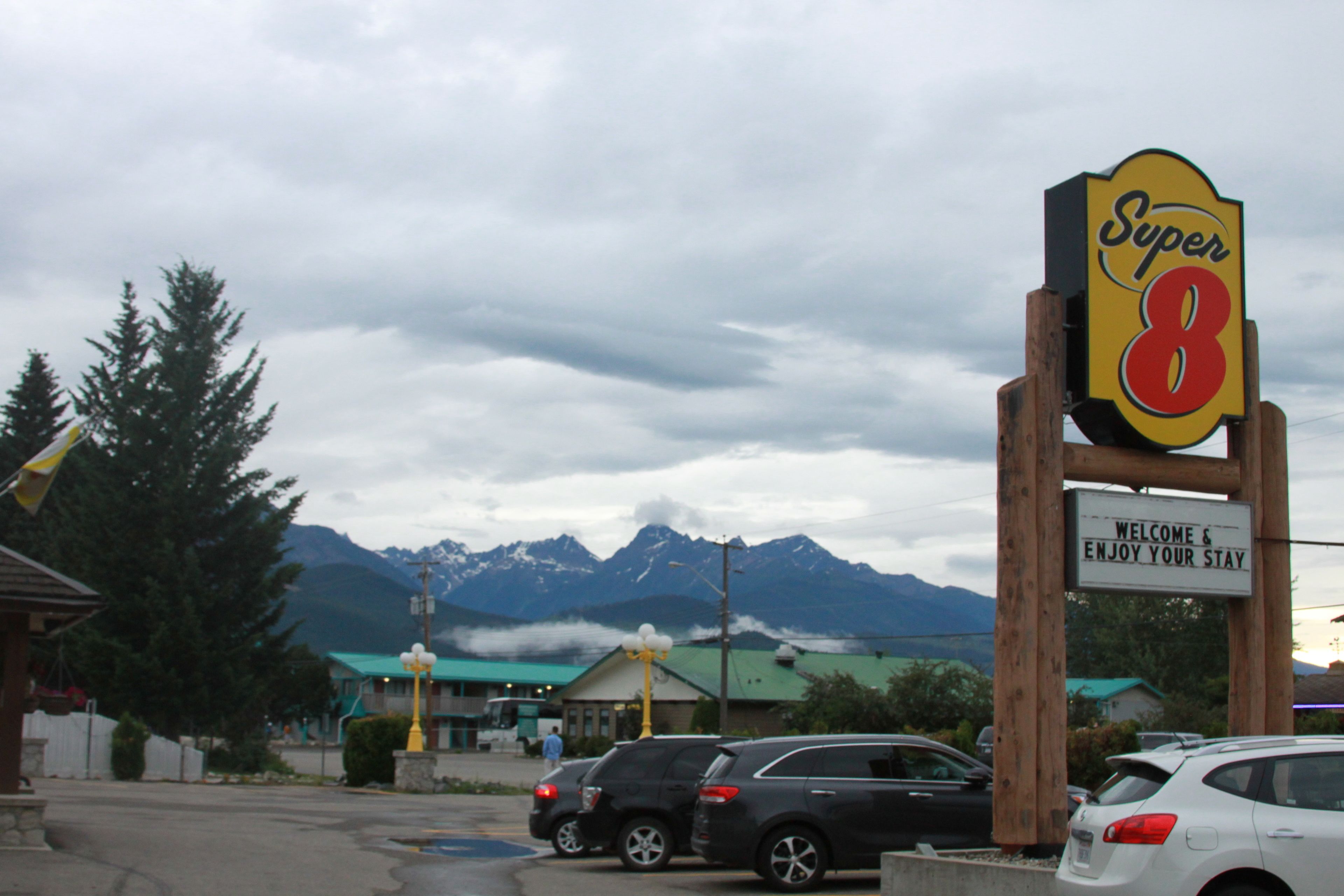 Placa Super 8 com uma mensagem acolhedora, carros estacionados em frente e montanhas ao fundo.