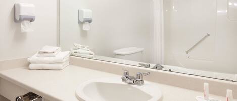 A modern bathroom with a sink, mirror, towel dispenser, and shower.