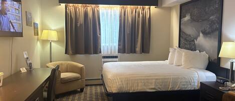 A hotel room with a bed, a desk, a chair, a TV, and a large painting on the wall.