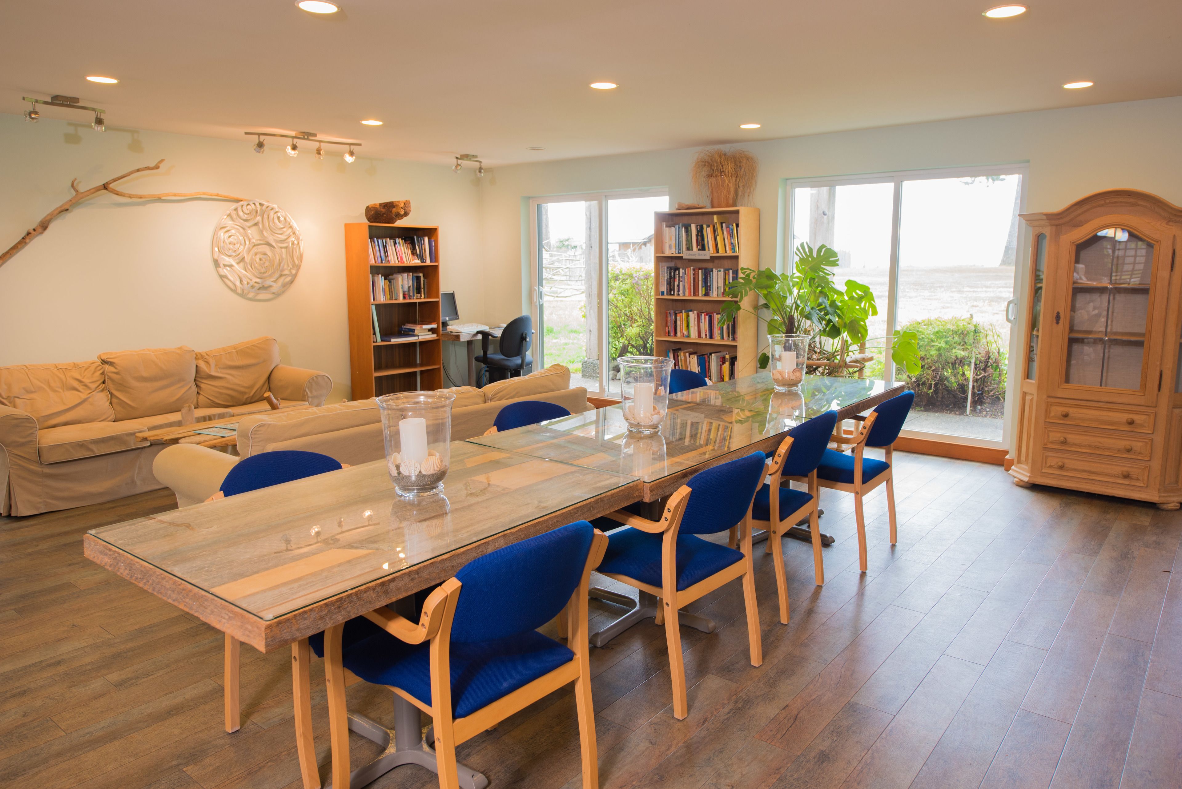 Un salon spacieux avec une grande table à manger en bois, des chaises bleues, un canapé beige et une bibliothèque.