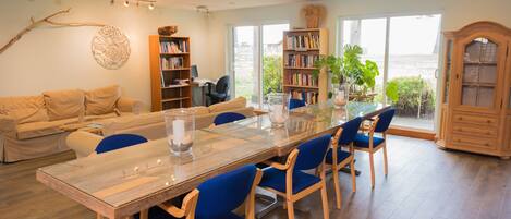Un salon spacieux avec une grande table à manger en bois, des chaises bleues, un canapé beige et une bibliothèque.