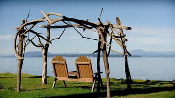 Una silla mecedora de madera bajo una estructura de arco rústico junto a un lago con montañas al fondo.