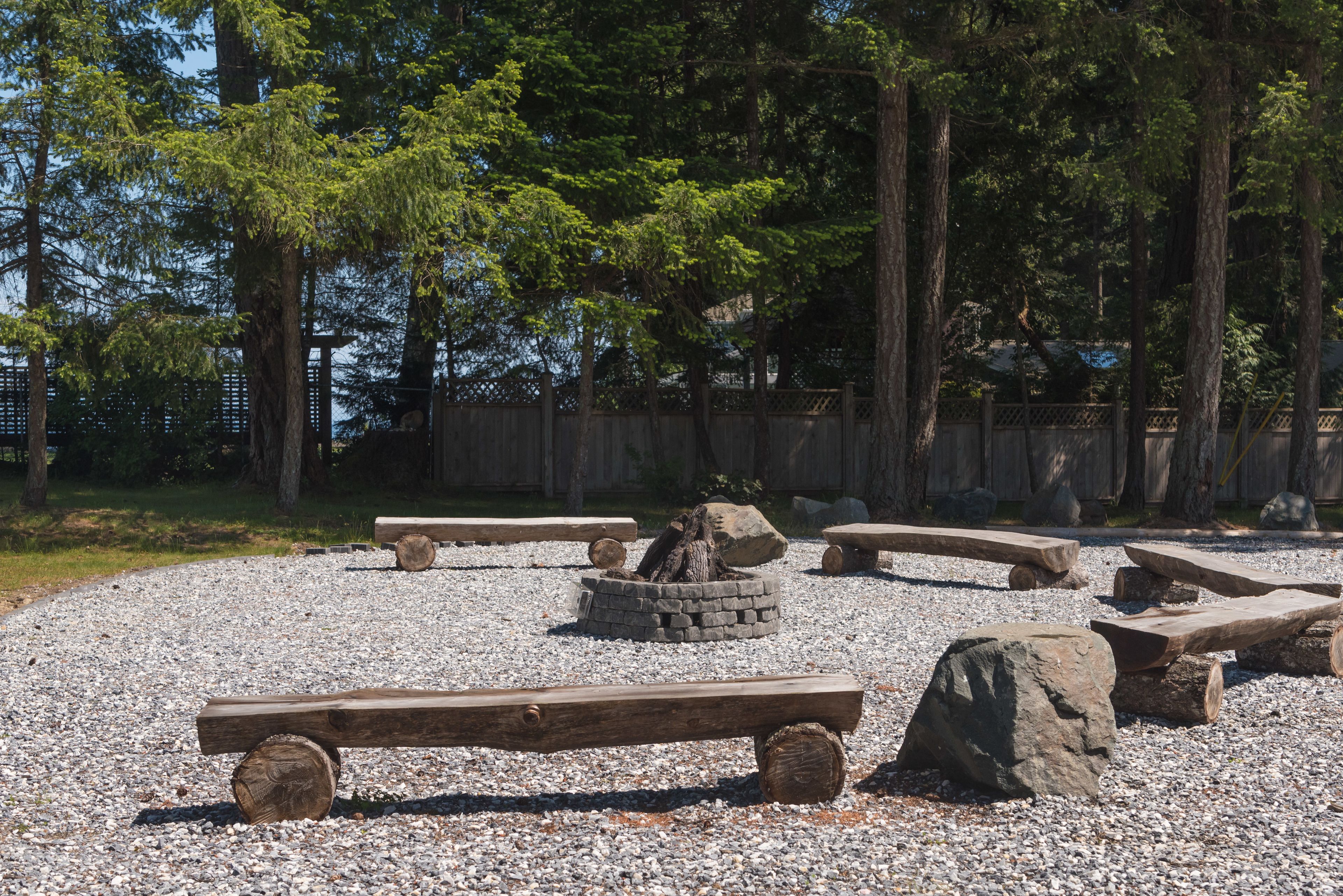 A gravel area with wooden benches and a fire pit.