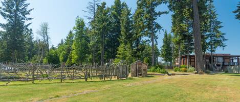 A rural landscape with a small wooden structure, a modern building, and tall trees.
