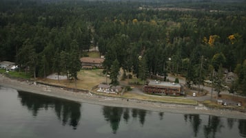 Vista aérea de una propiedad junto al lago con varias construcciones, incluyendo un gran edificio principal y casas más pequeñas, rodeadas de un bosque denso.