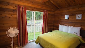 Un dormitorio de cabaña de madera con una cama, un ventilador y una ventana con cortinas.