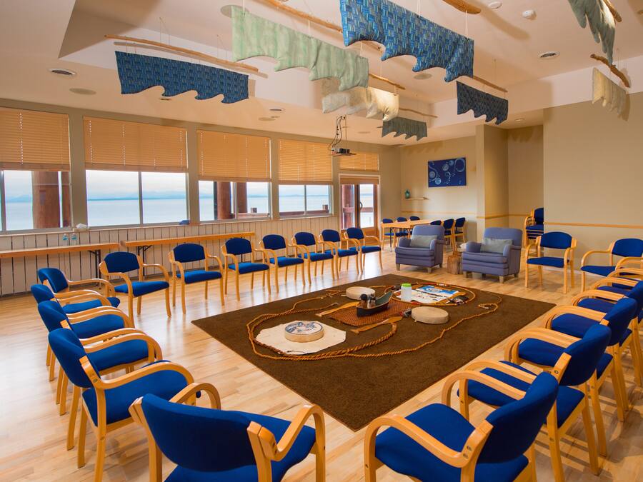 A conference room with rows of blue chairs, a central table with a rug, and large windows with a view.