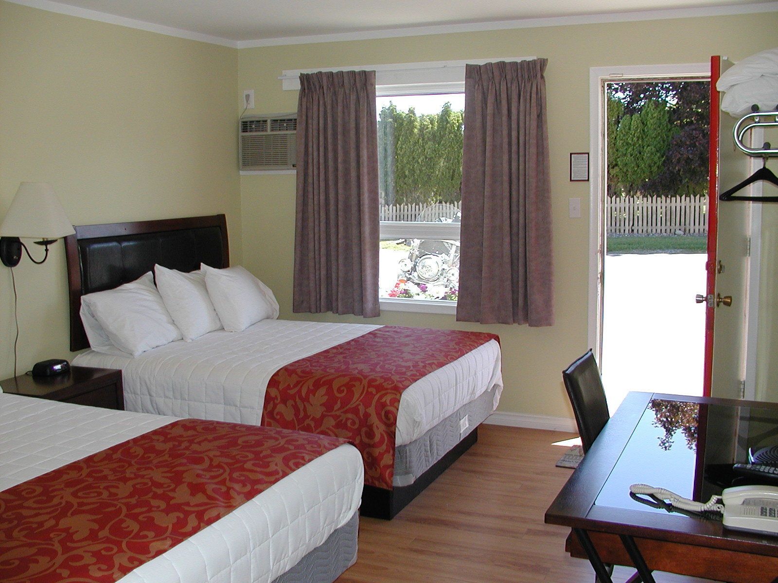 A hotel room with two beds, a desk, a chair, a telephone, and a window with curtains.