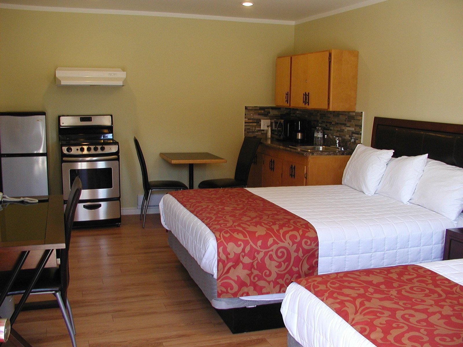 A hotel room with a bed, a desk with a chair, a kitchenette, and a refrigerator.