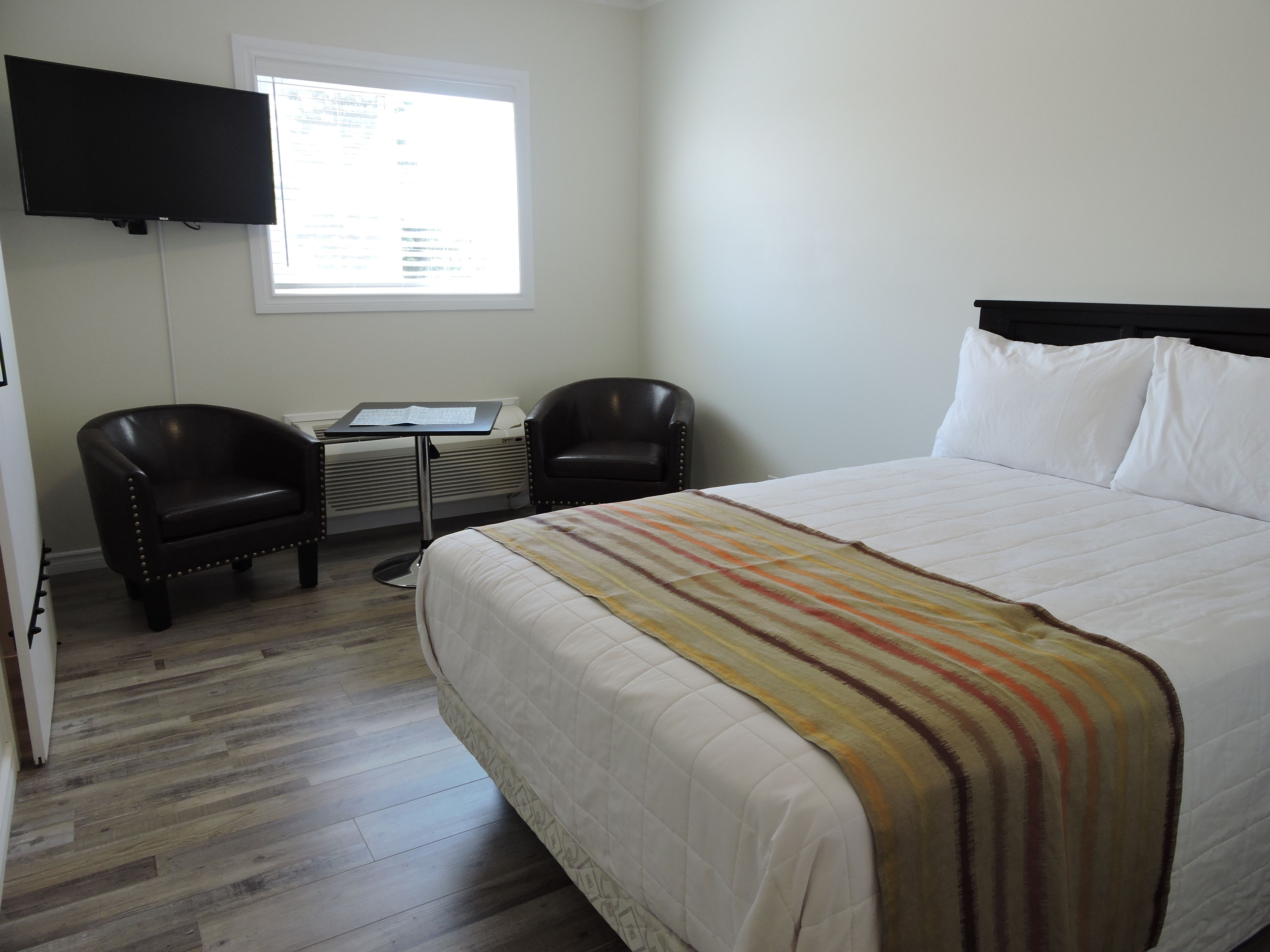 Habitación de hotel con una cama, dos sillas, un escritorio con computadora, una ventana y un televisor de pantalla plana en la pared.