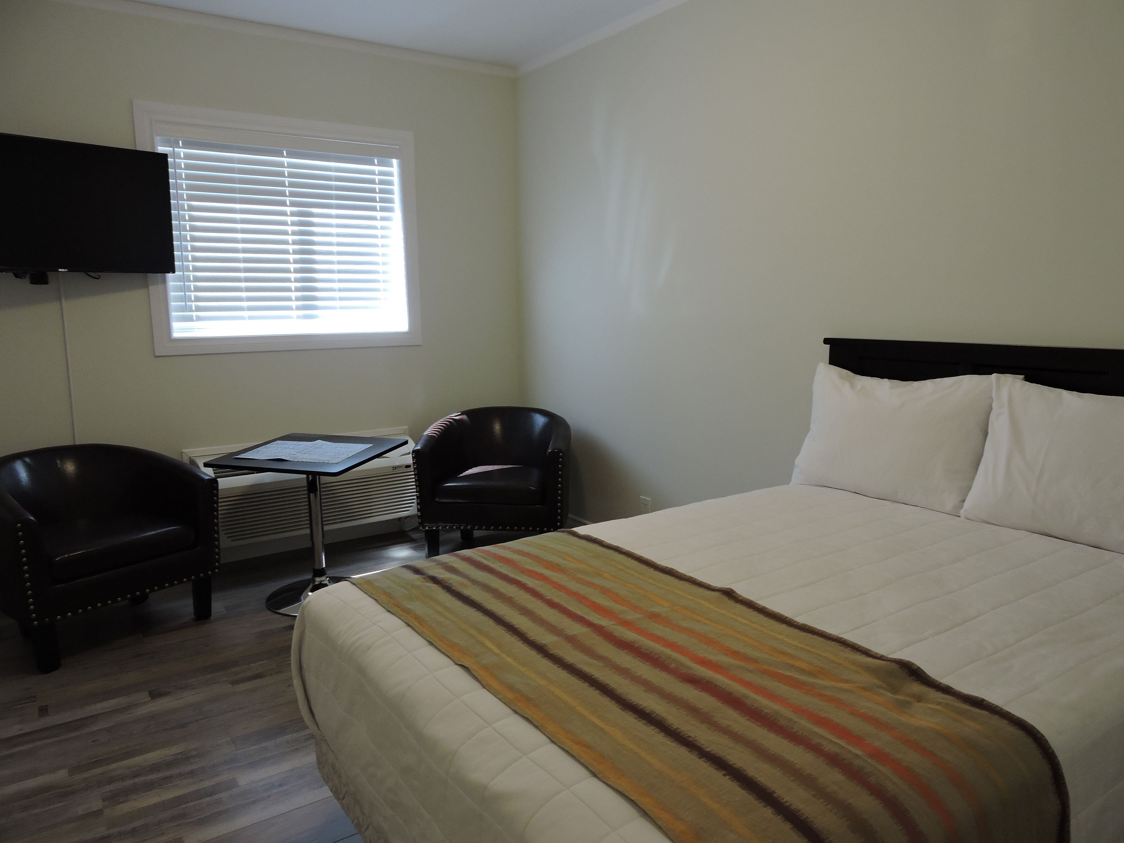 A hotel room with a bed, two chairs, a desk, and a TV mounted on the wall.