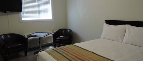 A hotel room with a bed, two chairs, a desk, and a TV mounted on the wall.