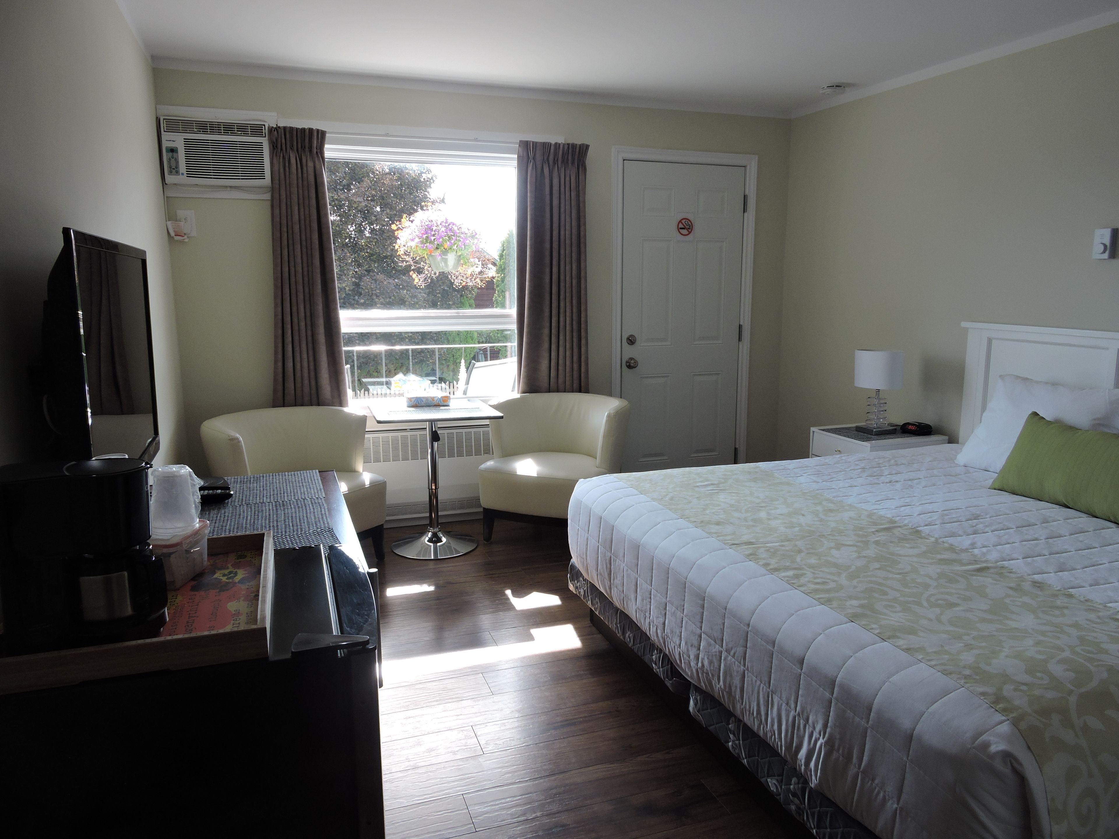 A hotel room with a bed, two chairs, a small table, a TV, and a window with curtains.