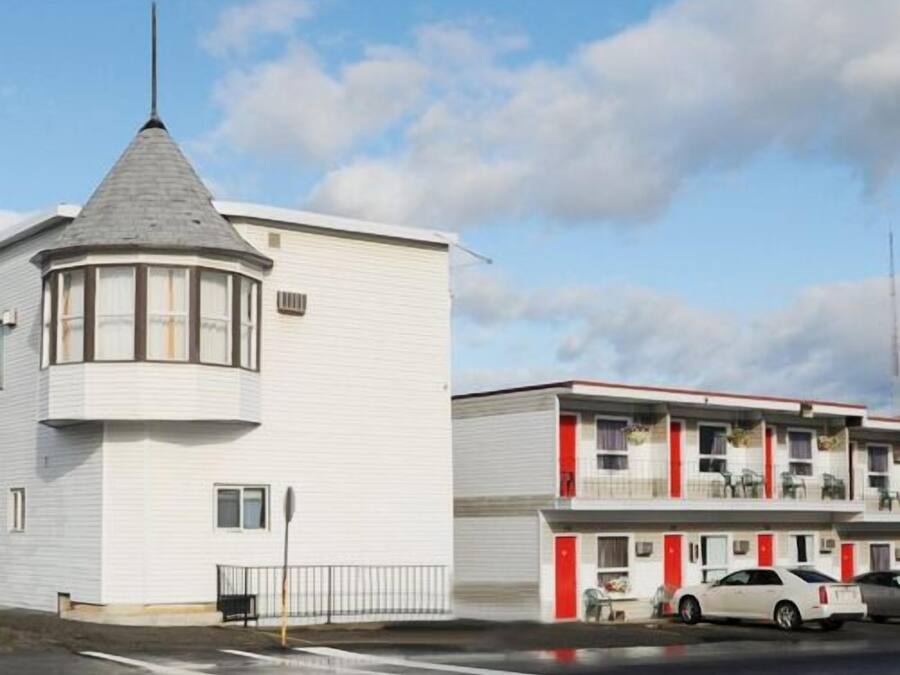 Un edificio blanco con techo cónico y torreta en una esquina. Junto a él, un edificio de varios pisos con detalles rojos y balcones.