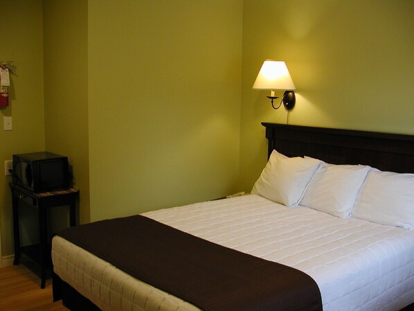 A hotel room with a bed, a nightstand, a lamp, and a television. - Almo Court Motel (Cranbrook)