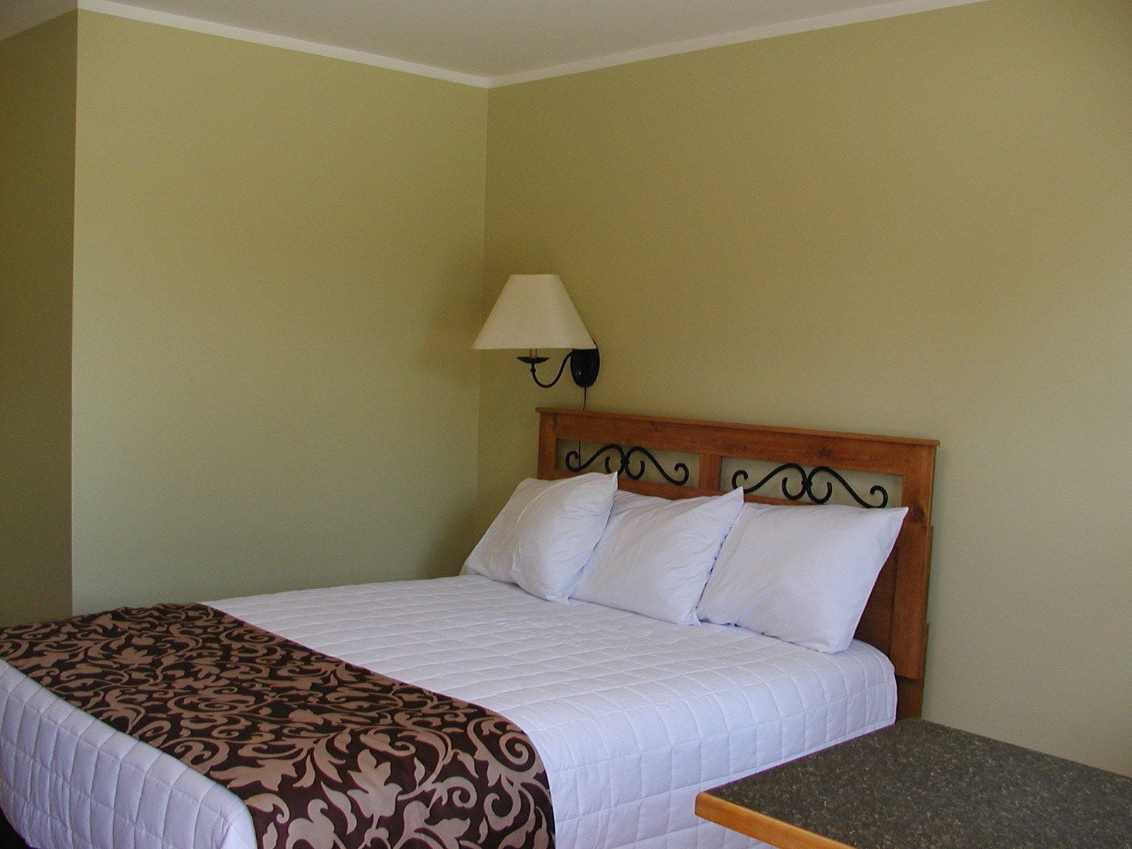 A neatly made bed with a patterned bedspread, a wooden headboard, and a nightstand with a lamp.