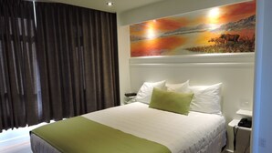 A hotel room with a large bed, a painting above the bed, a telephone, and a nightstand. - Almo Court Motel (Cranbrook)