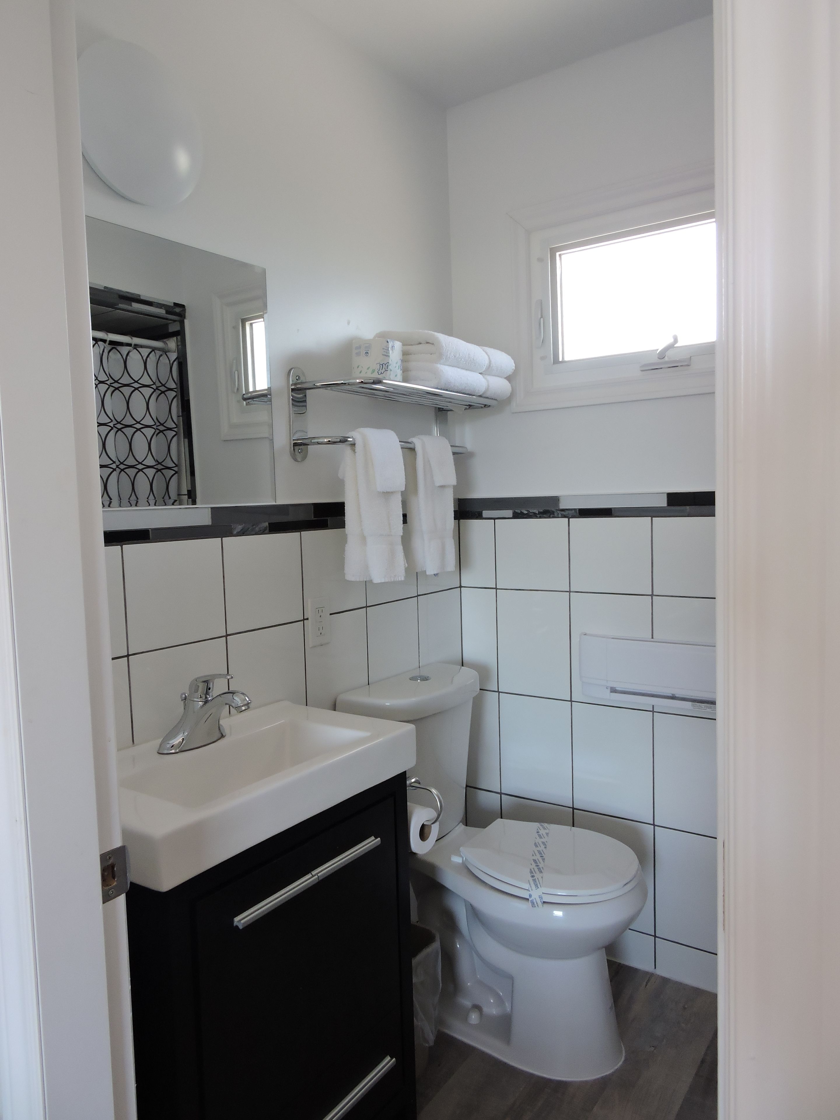 A modern bathroom with a white sink, black cabinets, a toilet, and a towel rack.