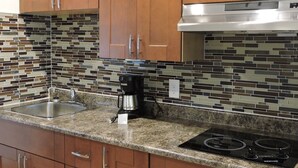 A kitchen with wooden cabinets, a stainless steel range hood, a coffee maker, and a tiled backsplash. - Almo Court Motel (Cranbrook)
