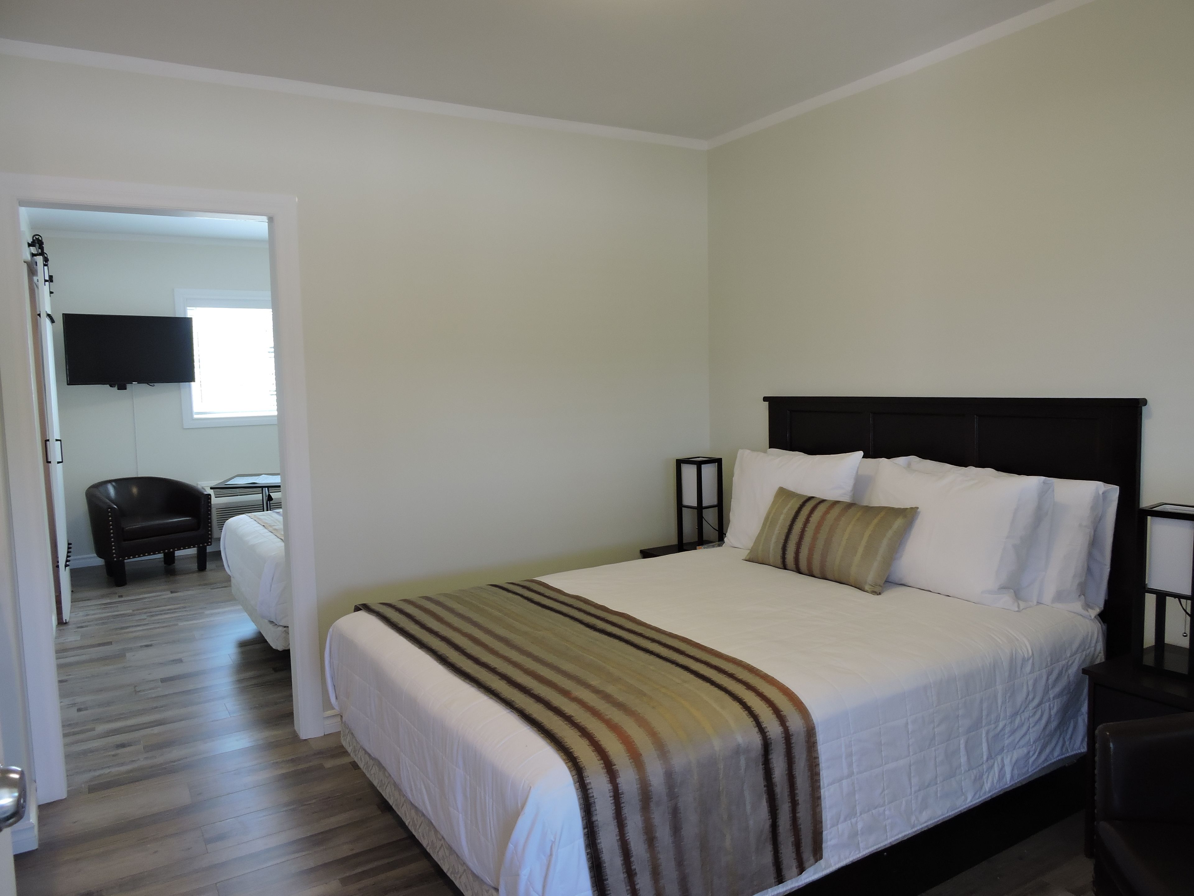 Une chambre d’hôtel bien rangée, avec un lit, une chaise, un téléviseur fixé au mur et une porte donnant sur une autre pièce.