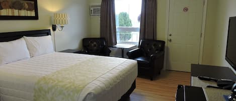 Habitación de hotel con una cama grande, dos sillones, una mesita, un televisor y una puerta con letrero de prohibido fumar.