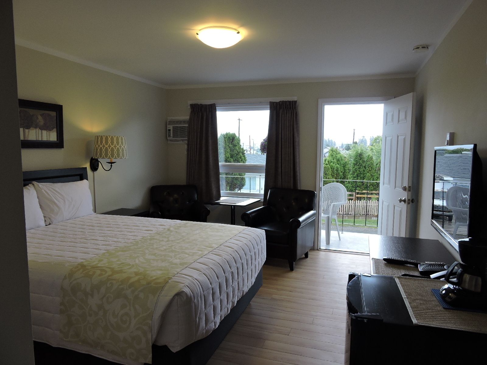 A hotel room with a bed, a desk, a chair, a TV, and a balcony with a view of the city.