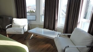 A hotel room with a bed, two white armchairs, a small table, and a window with curtains. - Almo Court Motel (Cranbrook)
