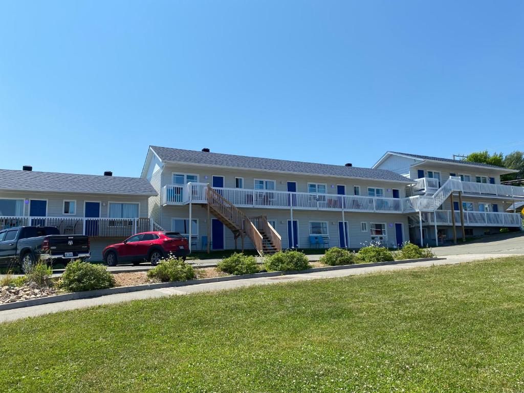 A multi-story motel with a central staircase, a parking area with two cars, and a grassy foreground.