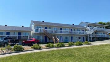 A multi-story motel with a central staircase, a parking area with two cars, and a grassy foreground.