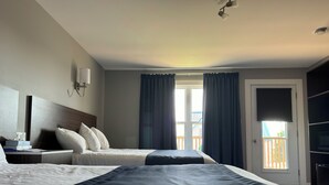 A hotel room with two beds, a large window with curtains, a door with a view, and a TV on the right. - Hotel Motel Fleur De Lys (Perce)