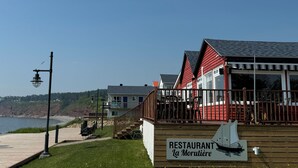A coastal restaurant with a wooden deck, a signboard, and a view of the sea. - Hotel Motel Fleur De Lys (Perce)