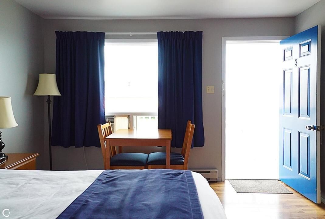 A hotel room with a bed, a table with chairs, a lamp, and a blue door.