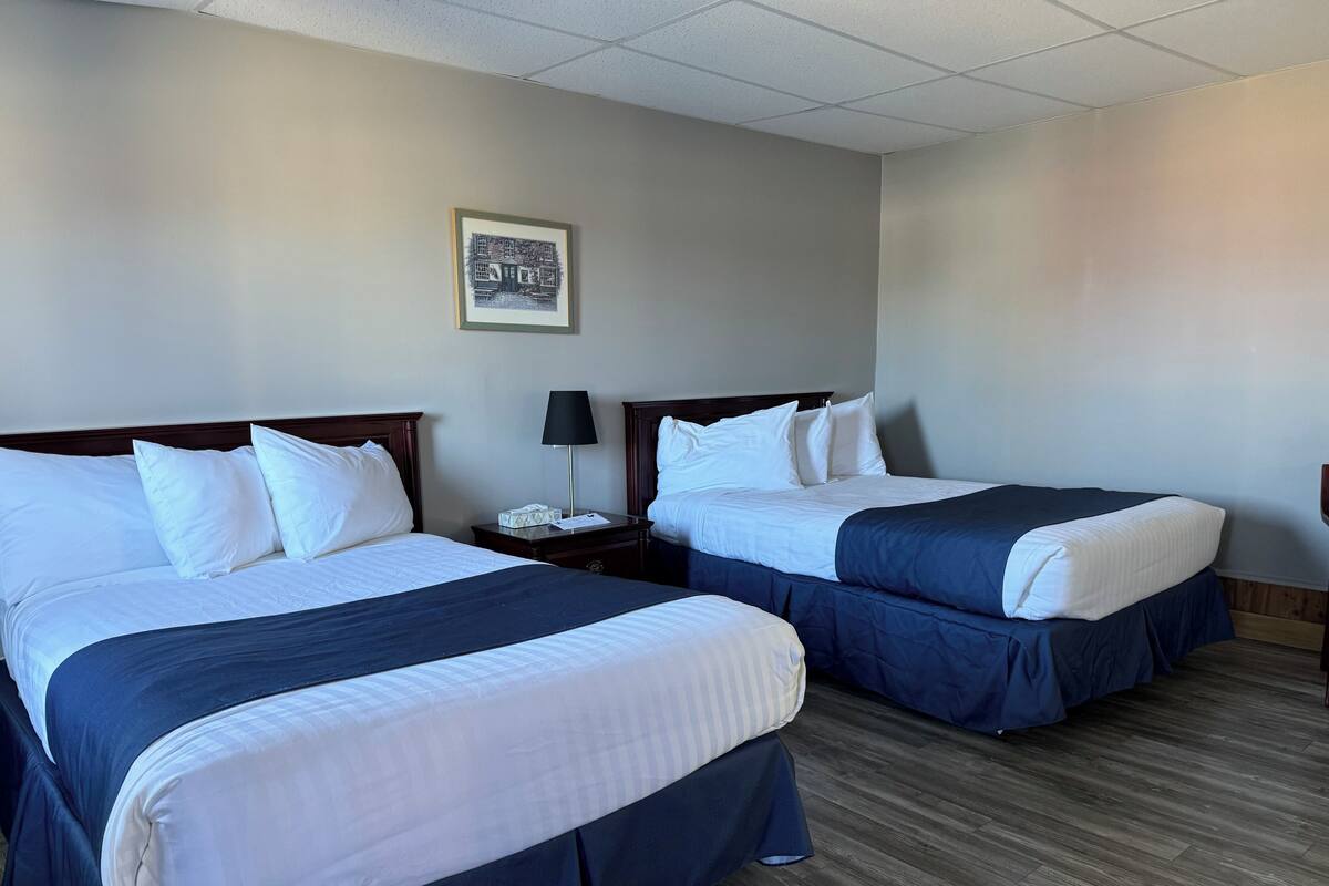 A hotel room with two beds, a nightstand with a lamp, and a framed picture on the wall.