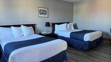Quarto de hotel com duas camas, uma mesa de cabeceira com abajur e um quadro na parede.