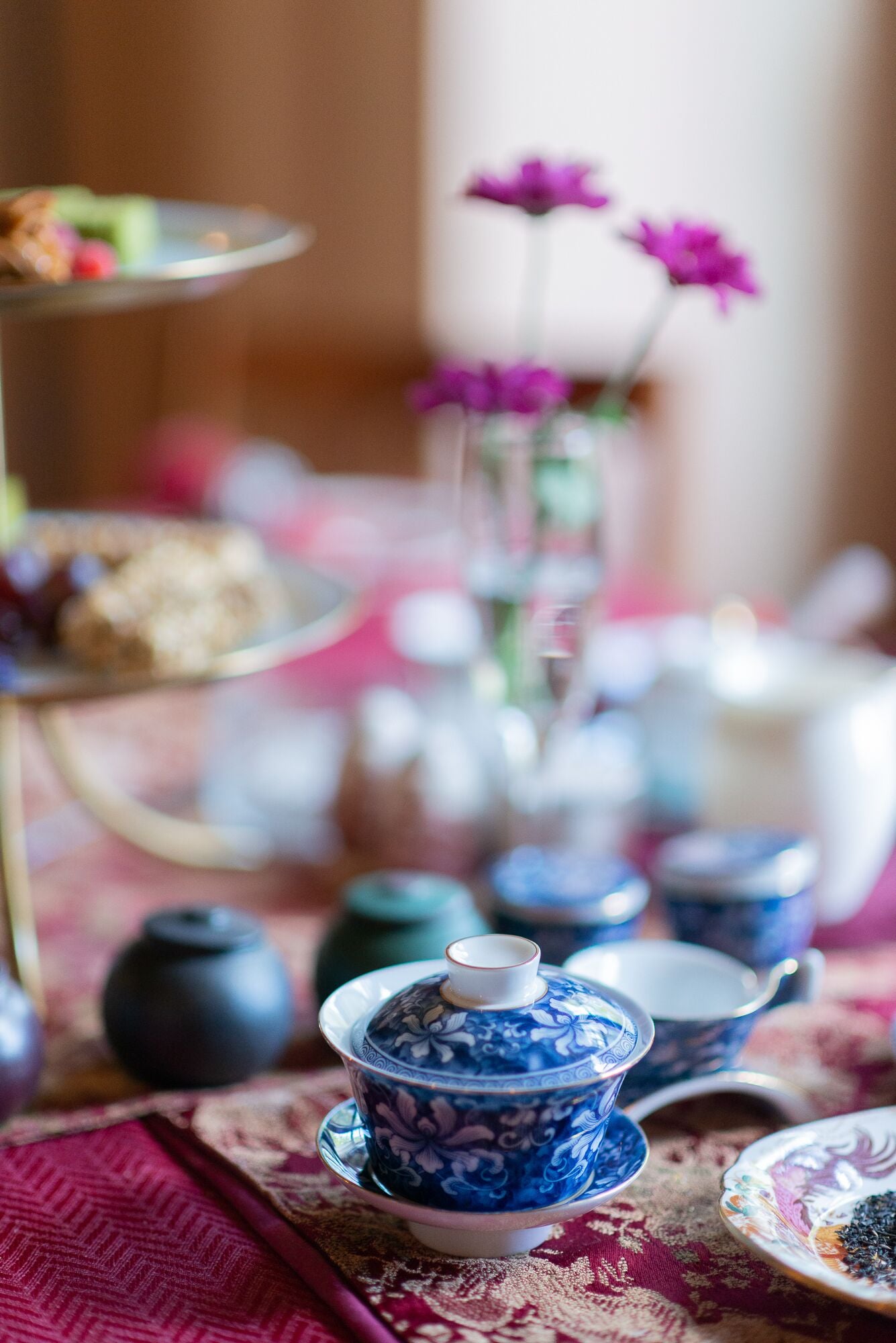 Une table avec des tasses à thé bleues et blanches, une théière et un présentoir à étages garni de pâtisseries.