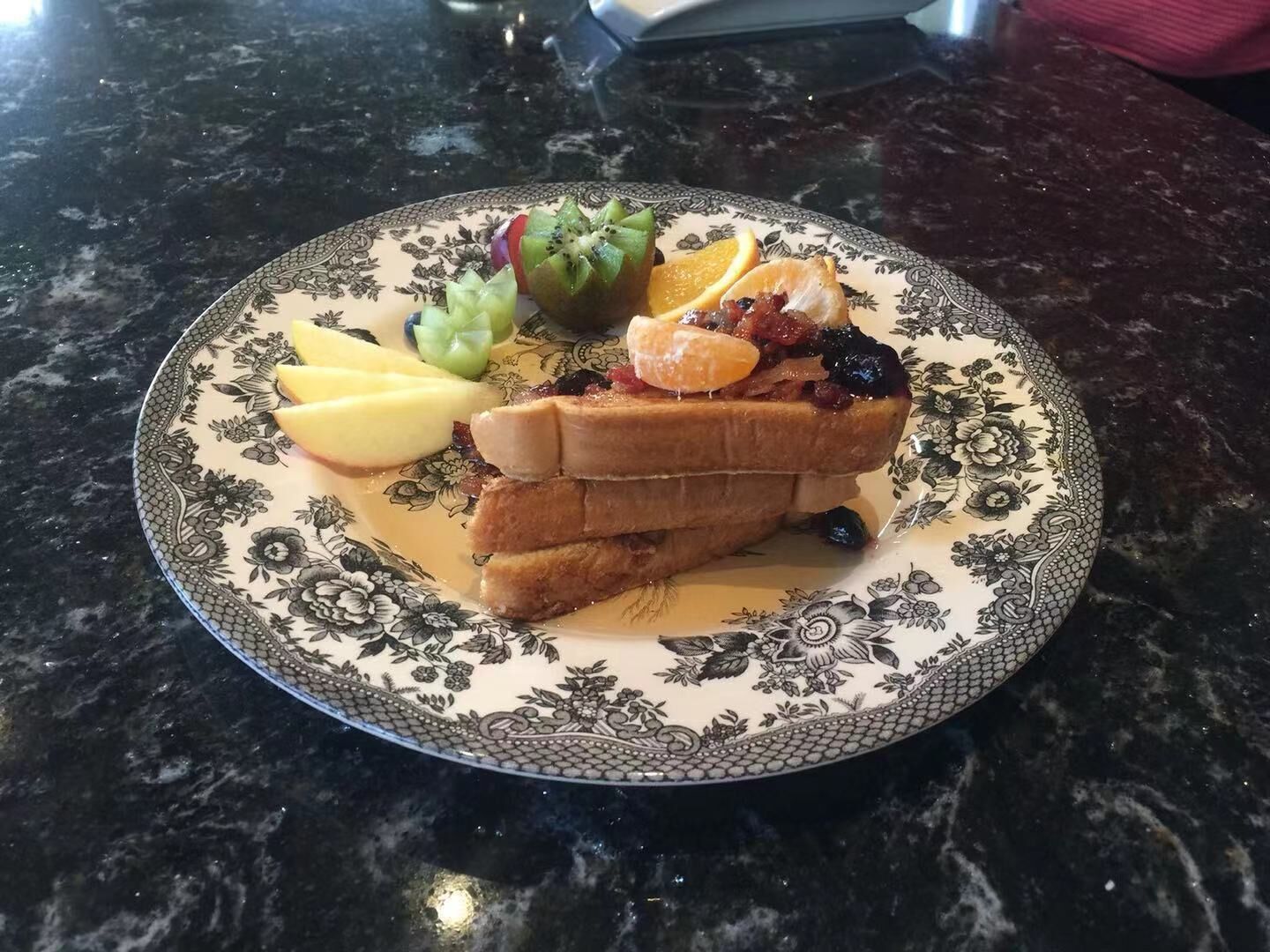 A plate of food with toast, fruit, and a small salad on a patterned plate.