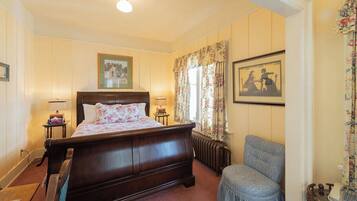 A traditional bedroom with a wooden bed, a chair, and two framed pictures on the wall.