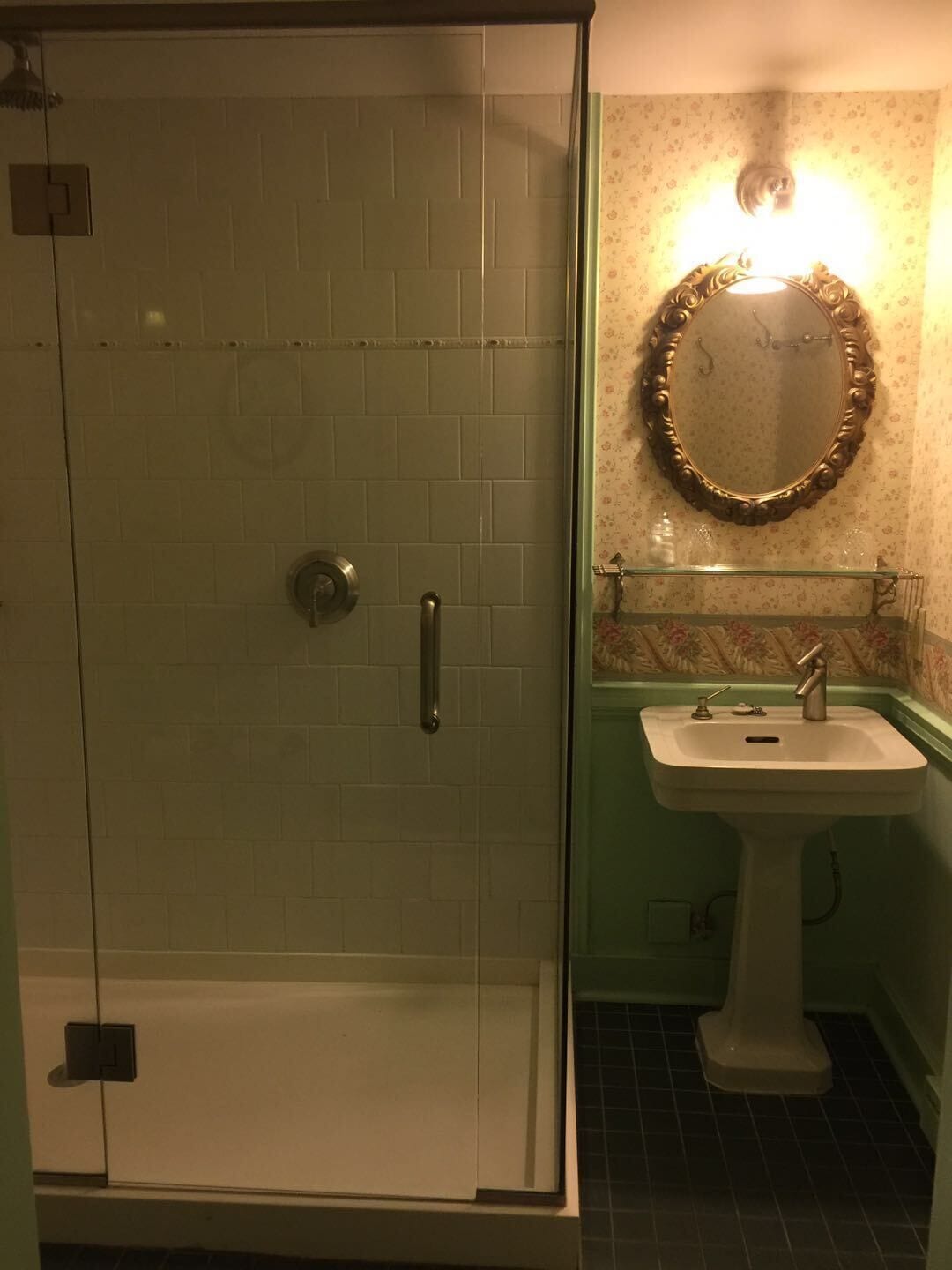 A bathroom with a glass shower enclosure, a pedestal sink, and a wall-mounted mirror.