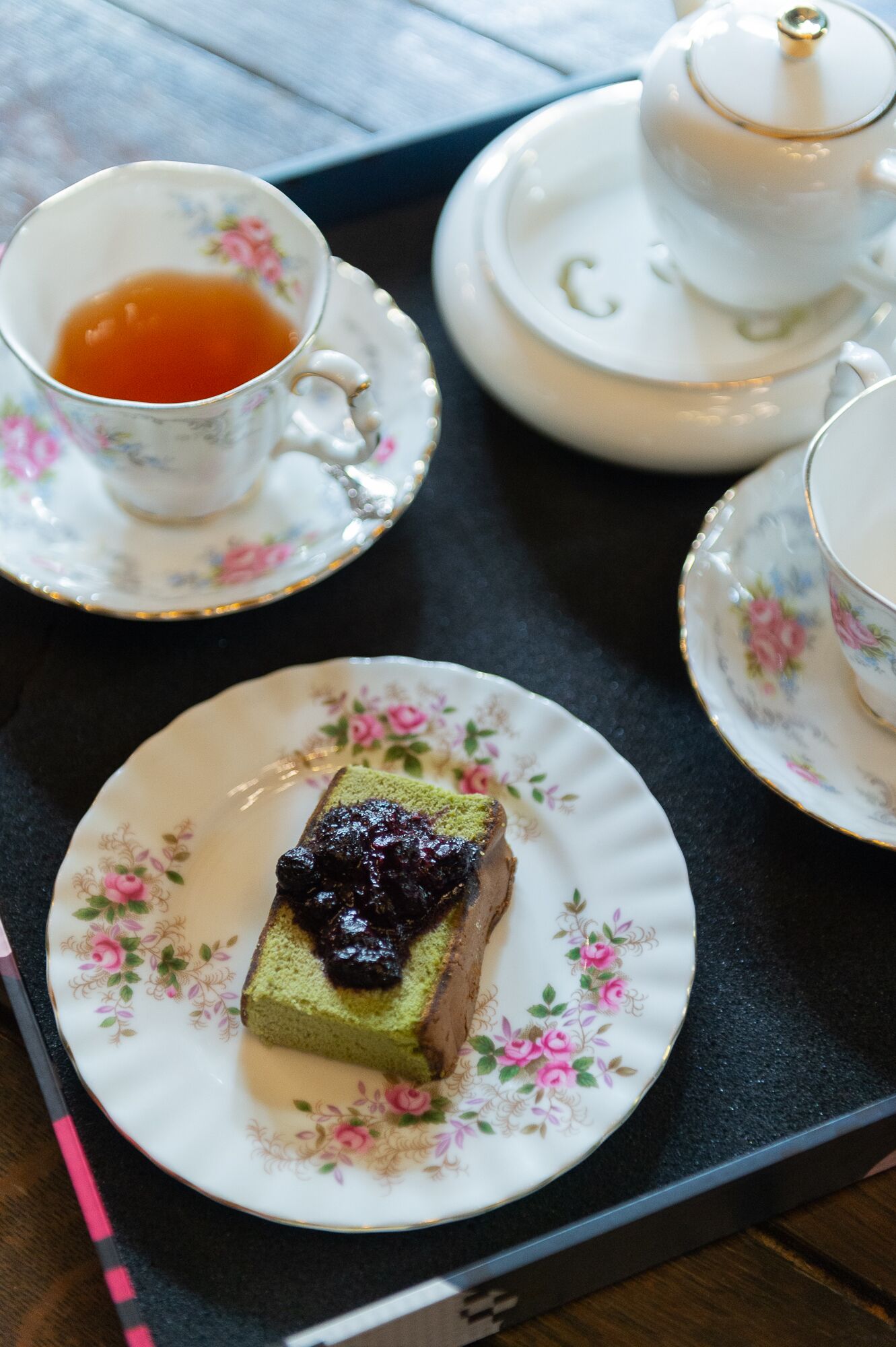 A tray with a teapot, teacups, and a slice of cake on a floral plate.