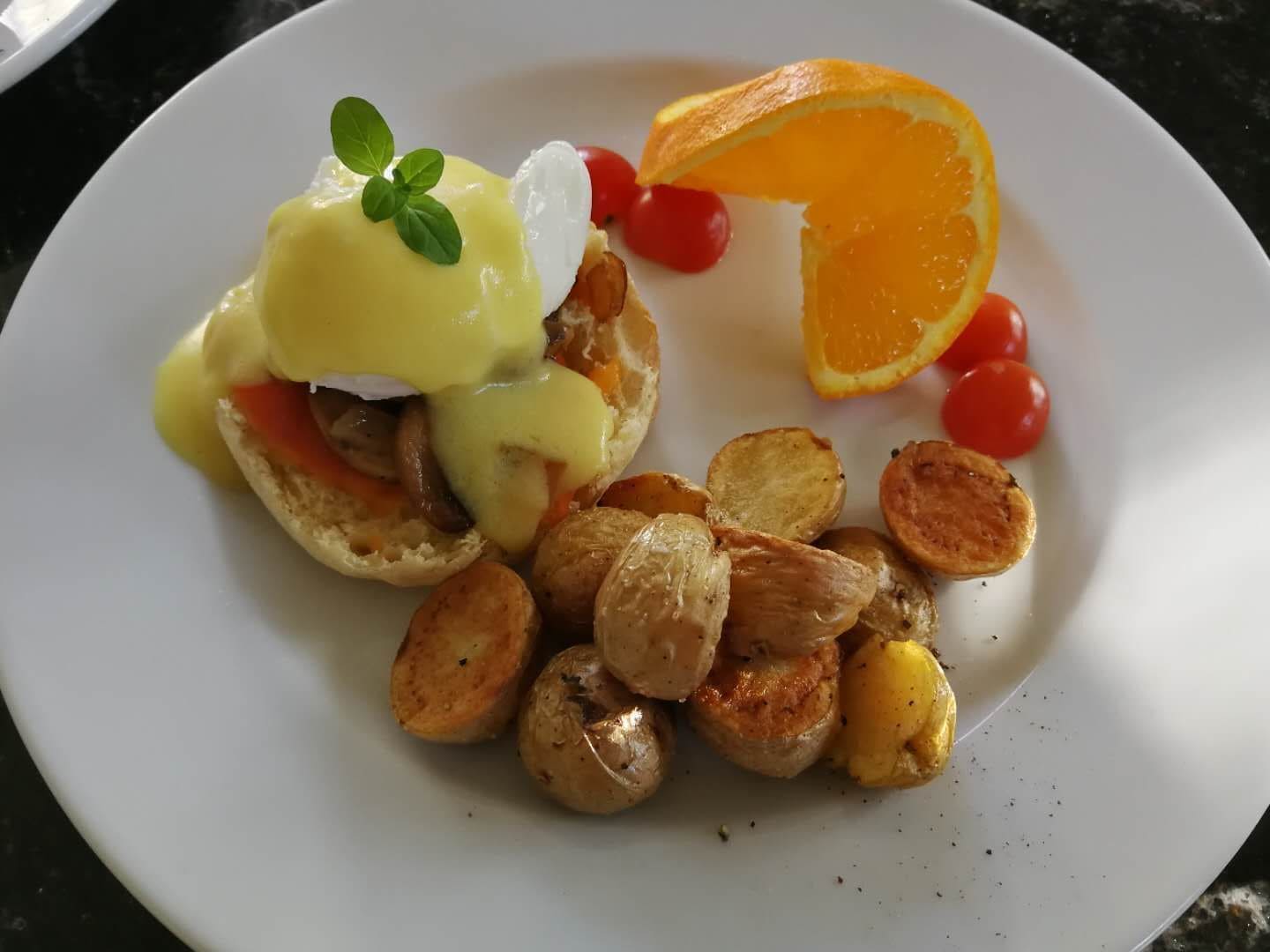 Une assiette contenant des œufs Bénédicte, des pommes de terre rôties et des tomates cerises.