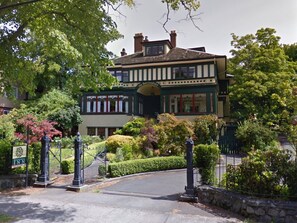 A two-story building with a traditional architectural style, featuring a prominent entrance with a gated driveway and manicured gardens. - Beaconsfield Inn (Victoria)