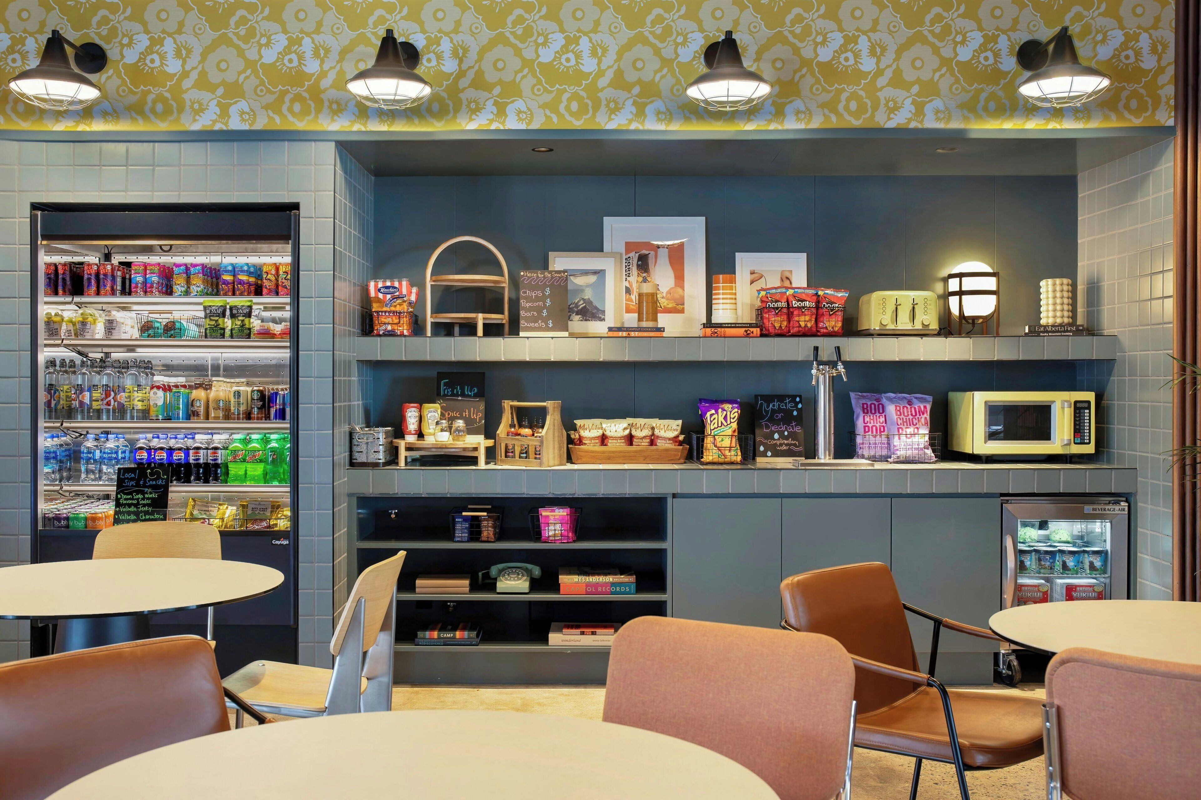 A cafe with seating, a beverage fridge, and various food items displayed on shelves.